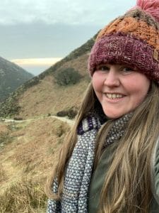 julie bickers headshot wearing scarf and woolly hat in winter with bridleway and hills in distance