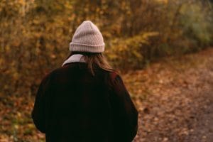 Julie Bickers wearing a beanie walks through a serene autumn forest path.